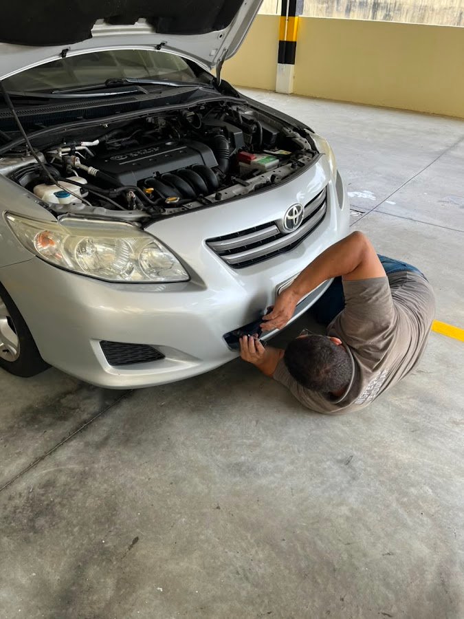 Inspetor deitado no chão verificando a parte de baixo de um carro prata
